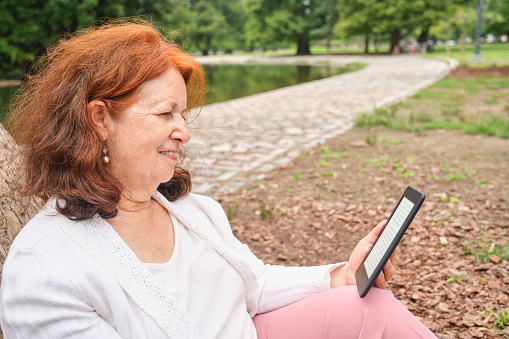 Mature hispanic woman reading an ebook on an electronic reader sitting in a park. Concepts: technology and reading. Image with copy space