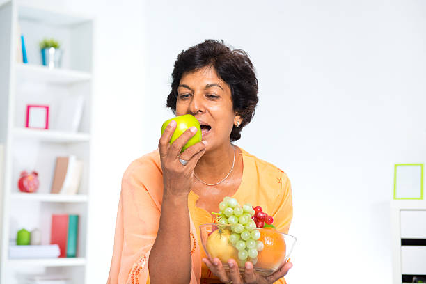 Mature Indian woman Mature 50s Indian woman eating fruits at home fruits stock pictures, royalty-free photos & images