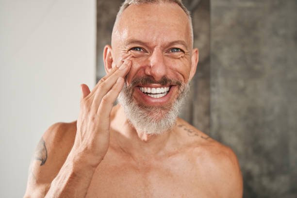 Mature man applying anti-aging cream on his face stock photo