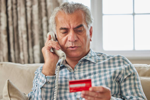 Mature Man At Home Giving Credit Card Details On The Phone stock photo