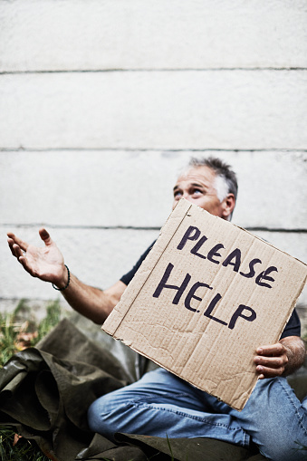 Beggar in his 50s asks for help with handwritten cardboard placard.