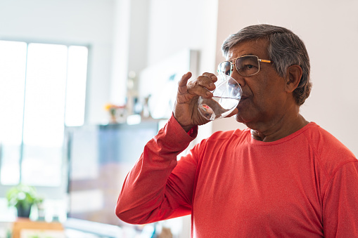 Senior man drinking water at home in the living room