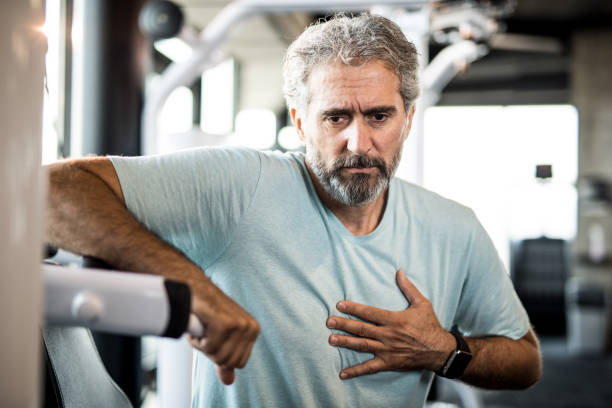 Mature man feeling chest pain while exercising in a gym. Mature man feeling chest pain while exercising in a gym. chest pain stock pictures, royalty-free photos & images