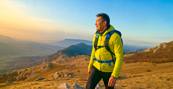 Smiling mature man looking away while walking on mountain trail against sky.
