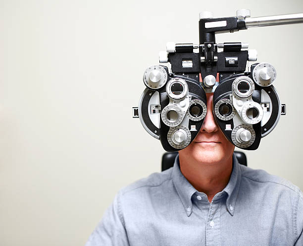Mature Man looking through Phoroptor Mature man looking through Ophthalmic Instrument called a phoroptor. optical instrument stock pictures, royalty-free photos & images