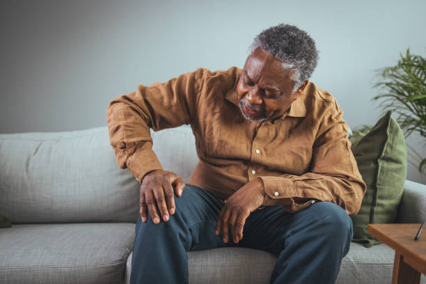 Mature man massaging his painful knee. Senior man holds his hands up to his knees, knee pain, arthritis, arthrosis, meniscopathy, tendonitis. The concept of medicine, massage, physiotherapy, health. sad old black man stock pictures, royalty-free photos & images