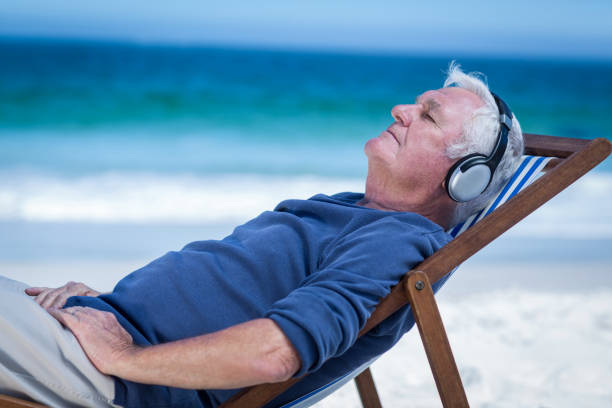 mogen man vilar på en vilstol som lyssnar på musik - senior listening music beach bildbanksfoton och bilder