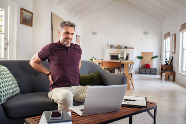 Mature man stretching back while working at home stock photo