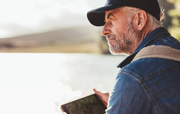 Mature man wearing cap sitting at a lake Close up portrait of mature man wearing cap sitting at a lake and looking at a view. Senior caucasian man with beard. mature men stock pictures, royalty-free photos & images