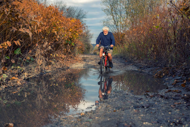 Mature men driving a bike in muddy dirt road stock photo