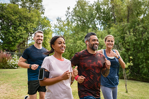 Healthy group of multiethnic middle aged men and women jogging at park. Happy mixed race couples running together. Mature friends running together outdoor.