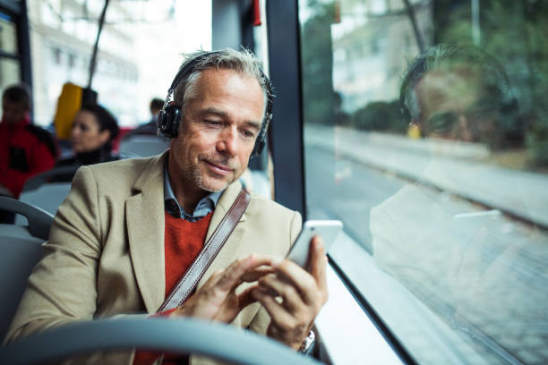 volwassen moe zakenman met heaphones en smartphone reizen per bus in de stad. - openbaar vervoer stockfoto's en -beelden
