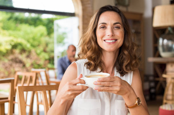 Mature woman at cafeteria Beautiful smiling woman drinking coffee at cafe. Portrait of mature woman in a cafeteria drinking hot cappuccino and looking at camera. Pretty woman with cup of coffee. brown hair stock pictures, royalty-free photos & images