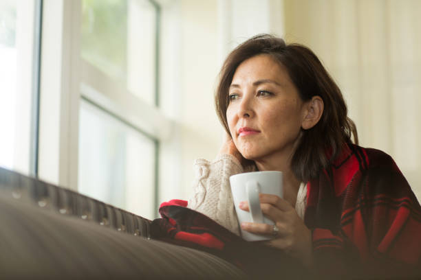Mature woman feeling sad looking out a window. stock photo