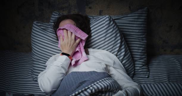 Mature woman is trying to sleep in bed but suffering from heat stock photo