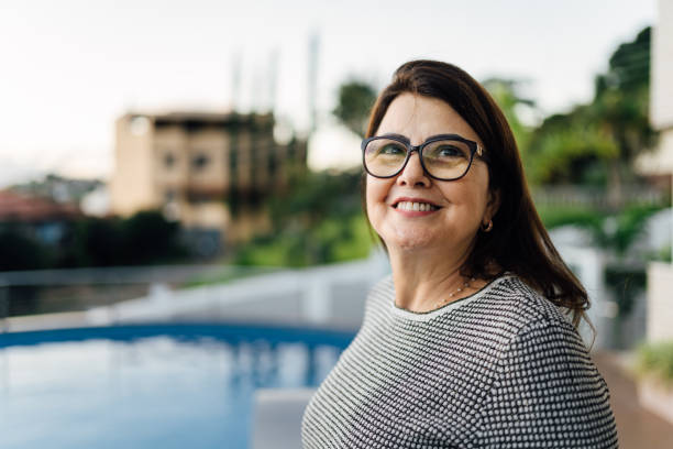Mature woman looking to the side in front a swimming pool Mature woman enjoying the view looking to the side in front her pool during mother's day. candid photos stock pictures, royalty-free photos & images