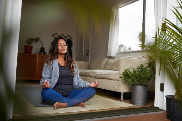 Mature woman meditating while practicing yoga in her living room Serene mature woman meditating with her eyes closed while practicing yoga on the floor of her living room at home meditating stock pictures, royalty-free photos & images