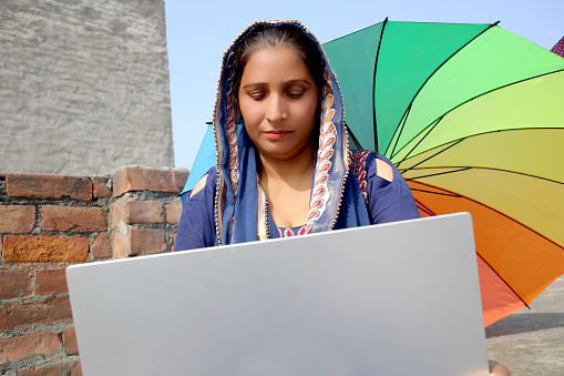 Serious Indian mature woman using computer outdoors on rooftop at home.