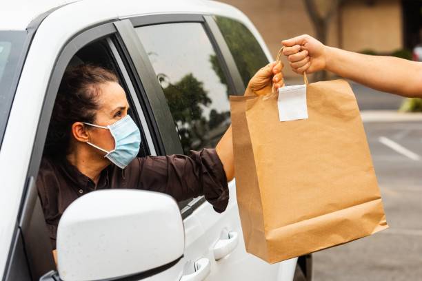 Mature woman picking her to go order from her car at a Curbside pickup Caucasian mature woman picking her to go order from her car at a Curbside pickup take out food stock pictures, royalty-free photos & images
