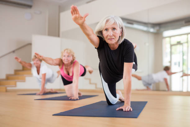 Mature woman practicing Dandayamna Bharmanasana during group yoga workout stock photo