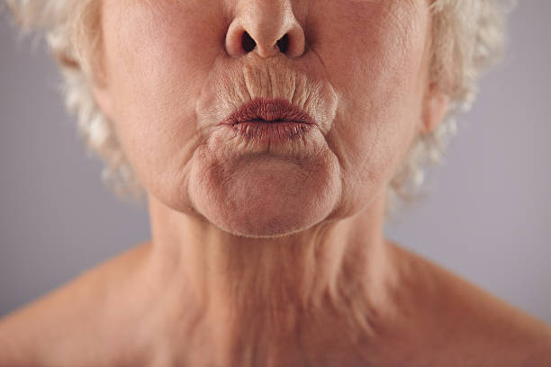 Mature woman puckering lips Close-up portrait of mature woman puckering lips against grey background. Senior woman grimacing. Focus on lips. ugly old women stock pictures, royalty-free photos & images