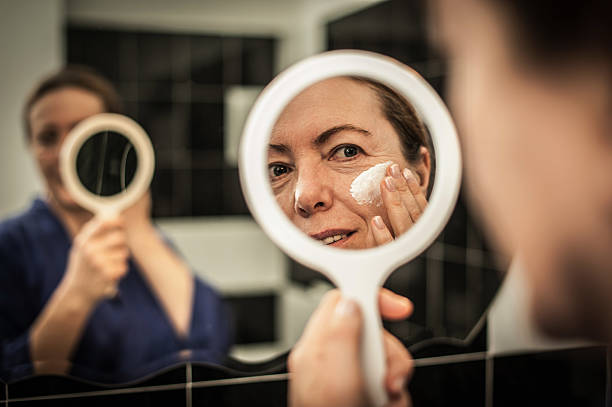 Mature Woman putting cream on her face stock photo