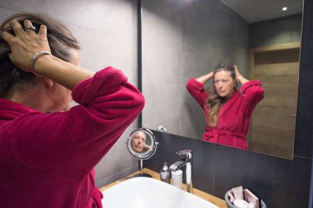 Mature Woman Reflecting Herself in the Bathroom Mirror stock photo