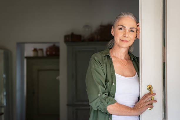 Mature woman standing at door Portrait of senior woman standing while leaning against door at home and looking at camera. Smiling mature woman standing at doorway and looking at camera. Portrait of old lady relaxing and thinking with copy space. mature women stock pictures, royalty-free photos & images