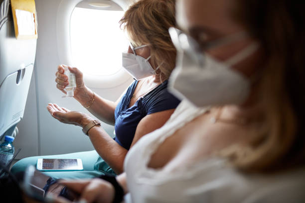Mature Woman Using Hand Sanitizer During Airplane Trip Side view with focus on background of woman in late 50s traveling with teenage daughter and squeezing sanitizer into her hand while flying in time of COVID-19. plane window seat stock pictures, royalty-free photos & images