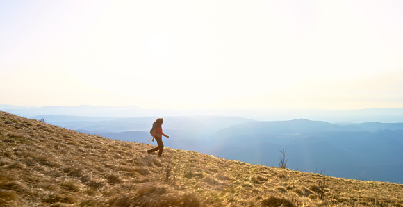 Side view of mature woman walking on mountain trail against mountain range and sky.