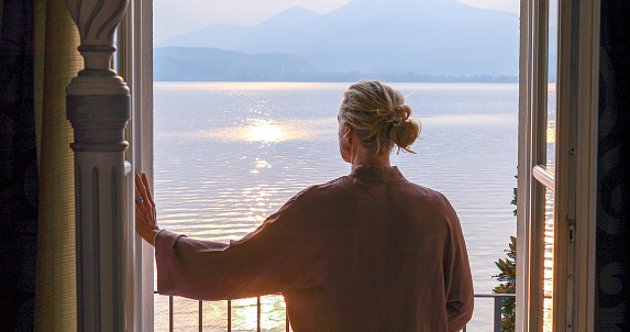 Mature woman walks out to veranda over a lake at sunrise