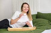 istock Mature woman with coffee mug sitting on edge of bed, portrait 1398827792