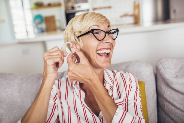 mujer madura con audífono en interiores sonriendo - hearing aids fotografías e imágenes de stock