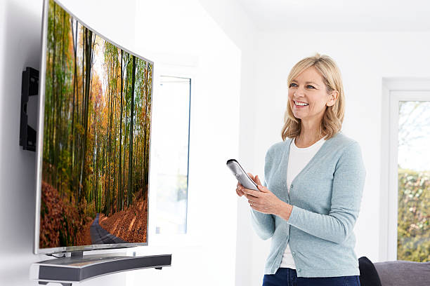 mature woman with new curved screen television at home - resolução 4k imagens e fotografias de stock