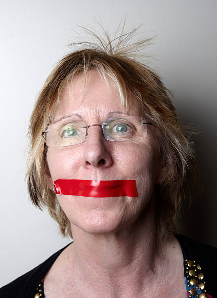 Mature woman with red tape over mouth Mature woman with red tape over mouth human mouth gag adhesive tape women stock pictures, royalty-free photos & images