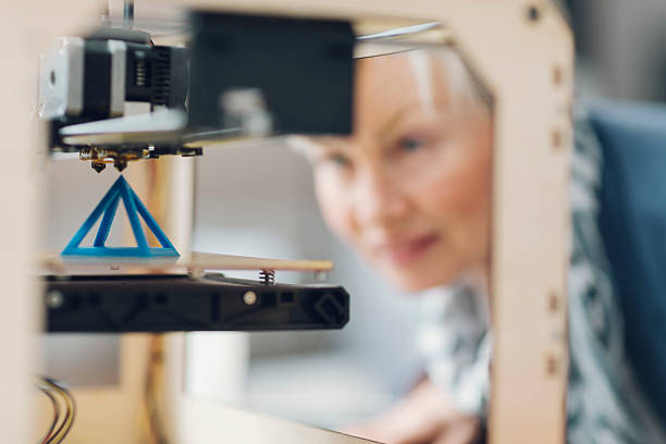 Mature Woman Working By 3D Printer in New Startup Office. Mature smiling woman working by 3d printer. Selective focus to object in the 3D printer. She is starting printing process for her new 3d project. 3d printing stock pictures, royalty-free photos & images