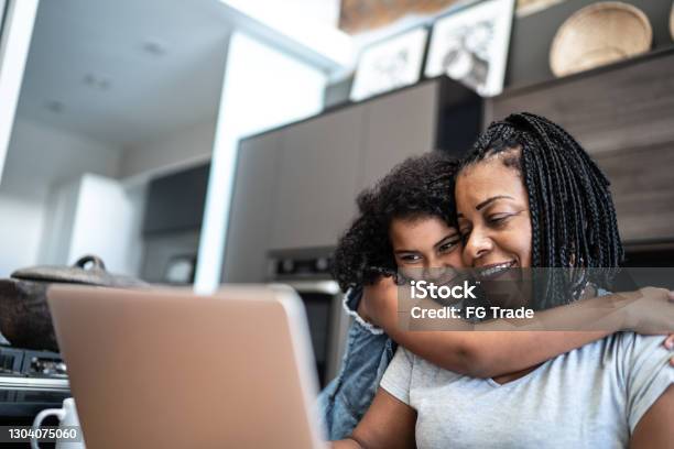 Mature woman working from home and being embraced by daughter