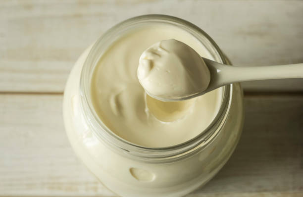Mayonnaise in a glass jar with a spoon on white wooden boards. stock photo