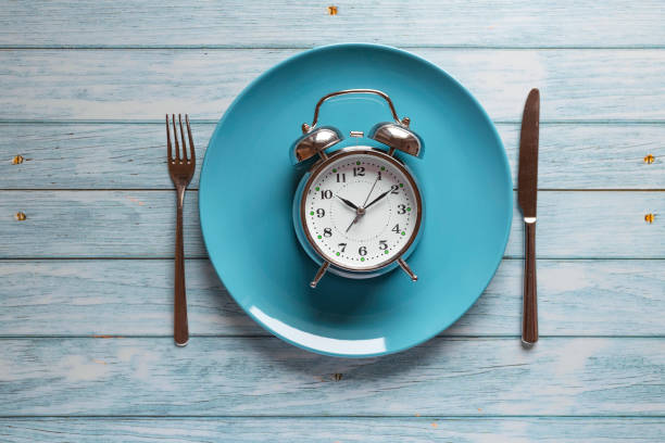Meal planning for diet concept, Intermittent fasting concept with clock on plate, fork and knife on wooden table, Clock on plate with fork and knife, intermittent fasting, meal plan, weight loss stock photo