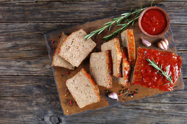 meatloaf cut in slices on board delicious meatloaf cut in slices with garlic, rosemary, and tomato sauce on cutting board on dark wooden table, view from above meatloaf stock pictures, royalty-free photos & images