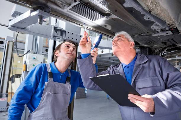 Mechanic And Male Trainee Working Underneath Car Together stock photo