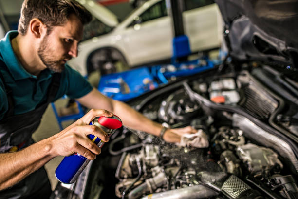 Mechanic cleaning and lubricating car engine with spray at repair shop. stock photo