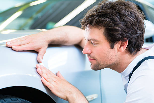 Mechanic controlling lacquer in car workshop Male mechanic examine car finish on dents or scratches in workshop dented stock pictures, royalty-free photos & images