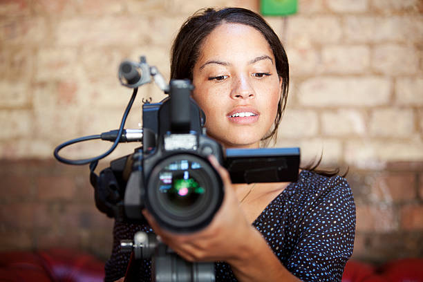 media: camera operator A look of content concentration on the face of a pretty camera operator pleased with the results of her shoot. camera operator stock pictures, royalty-free photos & images