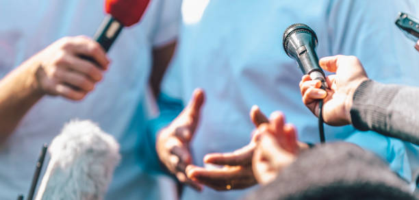 Media Event Outdoors. Journalists Interviewing Male Speaker Journalists interviewing male speaker and holding microphones and mobile phone. journalism stock pictures, royalty-free photos & images