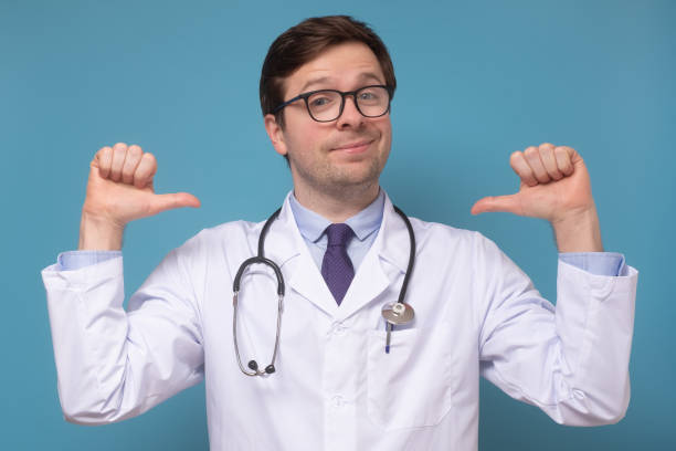 medical man intern or doctor feeling proud and self assured triumphing, being winner pointing at himself Caucasian young medical man intern or doctor feeling proud and self assured triumphing, being winner pointing at himself with thumbs tilting chest. Studio shot arrogance stock pictures, royalty-free photos & images
