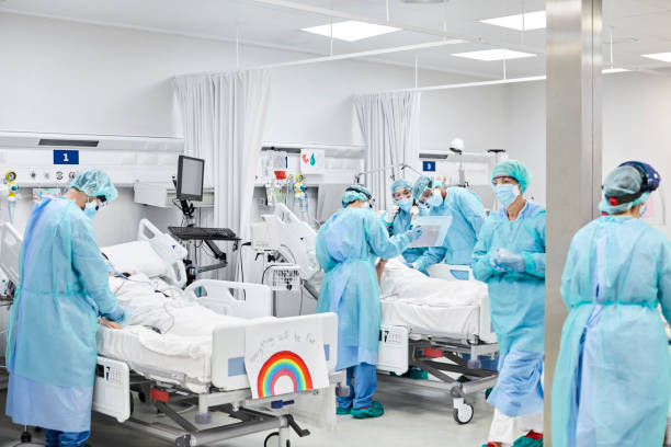 Medical Professionals Operating on Patient During Pandemic Medical professionals operating on patient in ICU. Doctors and nurses wearing protective coveralls. They are at hospital during pandemic. hospital ward photos stock pictures, royalty-free photos & images