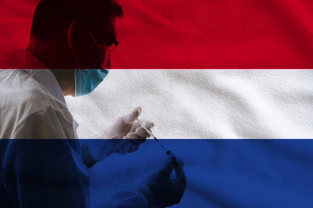 medisch onderzoeker met beschermend gezichtsmasker en handschoenen die coronavirus vaccinglas flacon en vulspuit van geneeskundeflet tegen de achtergrond van de vlag van nederland houden. - coronatest netherlands stockfoto's en -beelden