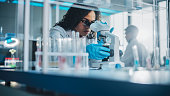 istock Medical Science Laboratory: Portrait of Beautiful Black Scientist Looking Under Microscope Does Analysis of Test Sample. Ambitious Young Biotechnology Specialist, working with Advanced Equipment 1346675527