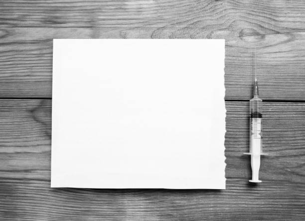 A medical syringe and blank sheet of paper on a wooden table. stock photo